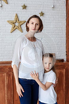 Cute little girl hugging her pregnant mother in studio