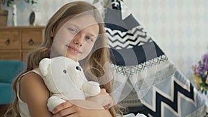 Cute little girl is hugging a teddy bear, looking at camera and smiling