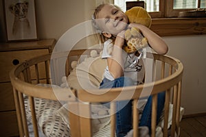 Cute little girl hugging teddy bear smiling while sitting on her bed at home