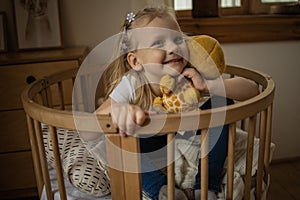 Cute little girl hugging teddy bear smiling while sitting on her bed at home