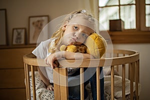 Cute little girl hugging teddy bear smiling while sitting on her bed at home