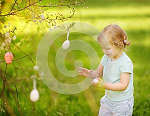 Cute little girl hunts for easter egg on branch flowering tree