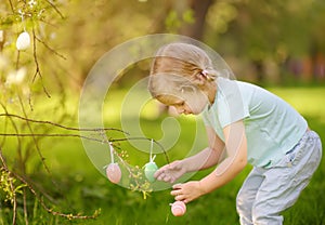 Cute little girl hunts for easter egg on branch of flowering tree