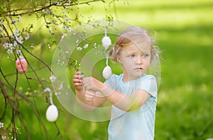 Cute little girl hunts for easter egg on branch flowering tree