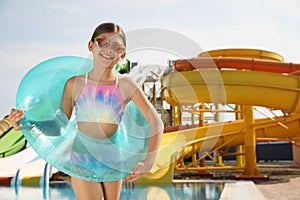 Cute little girl with inflatable ring near pool in water park, space for text