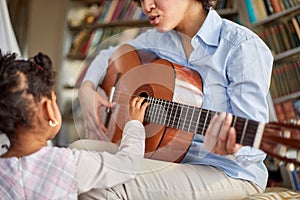 A cute little girl is so interested in her mother guitar playing while spending time at home together. Family, home, playtime