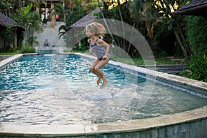 Cute little girl jumping in the swimming pool. Happy child playing in water. Summer concept. Kid activities. Happy childhood.