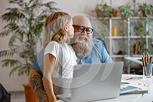 Cute little girl kisses smiling daddy thanking for help with homework in light room photo