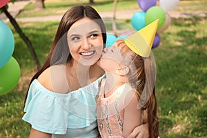 Cute little girl kissing her mother at birthday party outdoors