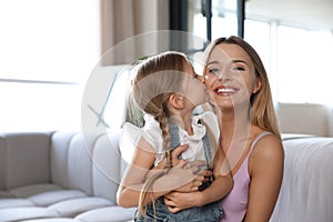 Cute little girl kissing her mother on sofa in room