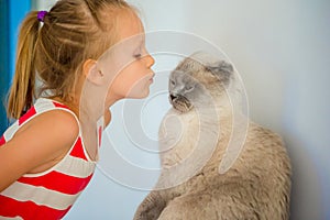 Cute little girl kissing her pet cat at home. Love between kid and pet