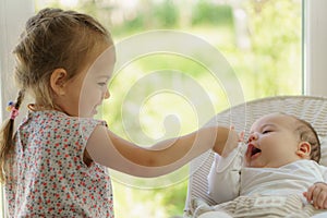 Cute little girl kissing his newborn sister. Toddler kid meeting new born sibling. Infant sleeping in white bouncer