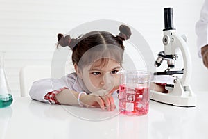 Cute little girl in lab coat doing science experiment at class room, young schoolgirl scientist kid having fun in chemistry