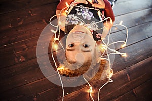 Cute little girl laying on flor with bright christmas garland in her hair