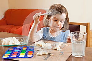 Cute little girl learning to paint dough figurines