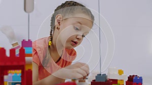 Cute little girl lies on carpet and playing with colorful lego building blocks