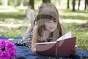 Cute little girl with lies on the grass and reading a book