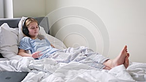 Cute Little Girl Listen To Music In Headphones Lying On The Bed In The Morning