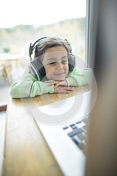 Cute little girl listening to music on headphones while using laptop at home