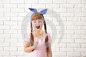 Cute little girl with lollipop near white brick wall