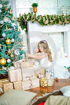 Cute little girl with long curly blond hair at home near a Christmas tree with gifts and garlands