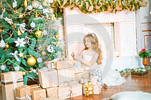 Cute little girl with long curly blond hair at home near a Christmas tree with gifts and garlands