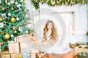 Cute little girl with long curly blond hair at home near a Christmas tree with gifts and garlands