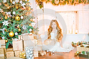 Cute little girl with long curly blond hair at home near a Christmas tree with gifts and garlands