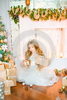 Cute little girl with long curly blond hair at home near a Christmas tree with gifts and garlands