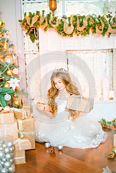 Cute little girl with long curly blond hair at home near a Christmas tree with gifts and garlands