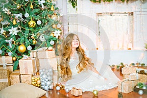 Cute little girl with long curly blond hair at home near a Christmas tree with gifts and garlands