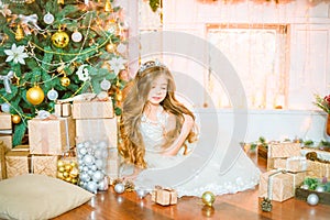 Cute little girl with long curly blond hair at home near a Christmas tree with gifts and garlands