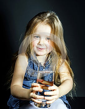 Cute little girl with long hair holding glass of water