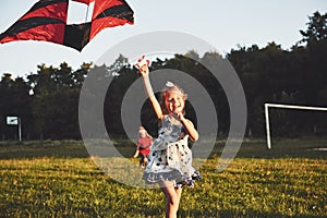 Cute little girl with long hair running with kite in the field on summer sunny day