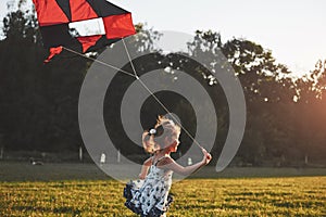 Cute little girl with long hair running with kite in the field on summer sunny day