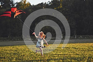 Cute little girl with long hair running with kite in the field on summer sunny day