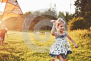 Cute little girl with long hair running with kite in the field on summer sunny day