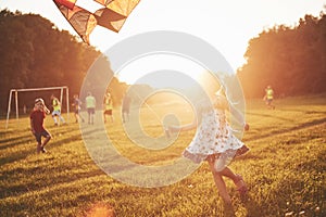 Cute little girl with long hair running with kite in the field on summer sunny day