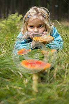 Cute little girl looking at mushrooms in summer - autumn forest