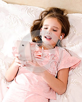 Cute little girl lying on the bed listening to music and singing