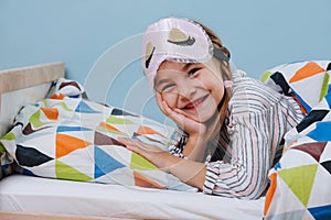 Cute little girl lying in bed with a sleeping mask on her forehead