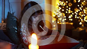 Cute little girl is lying on bed and write letter to Santa in room decorated for christmas, christmas eve