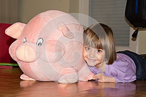 Cute little girl lying on the floor with her stuffed toy pig