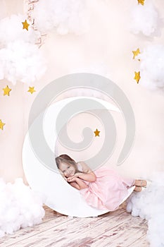 Cute little girl lying on the moon in anticipation of a miracle. Girl on the decorative moon on a background of stars. Sweet dream