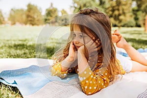 Cute little girl lying and relaxing on the blanket at the green grass. Beautiful child taking rest outdoors during picninc with