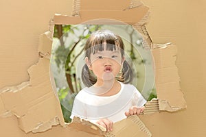 Cute little girl making funny faces in torn paper wall