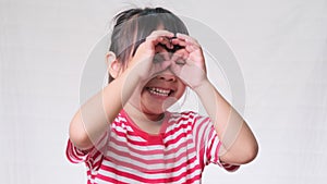 Cute little girl making funny faces wearing fingering glasses, shaped like looking through binoculars over a white studio backgrou