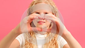 Cute little girl making heart with her hands and smiling on pink background. Young beautiful girl smiling in love