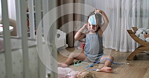 Cute little girl in medical mask with stethoscope playing doctor with toys at home floor.