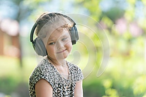 Cute little girl in modern wireless headphones enjoys music outdoors